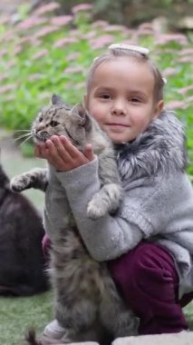 Neşeli bir kız, tüylü kedisini güzel doğal bir zemin üzerinde tutar, yürek ısıtan bir anı yakalar. Ağır çekim. Dikey video. Yüksek kalite 4k görüntü