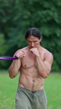 Çıplak vücutlu bir adam, yazın antrenman yapıyor, boks yapıyor. Canlı bir açık hava ortamında, tutkulu bir fitness meraklısı bir dizi dinamik direniş bandı egzersizi sergiliyor. Ağır çekim. 4k