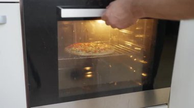 Bir el, canlı malzemelerle fırında lezzetli bir pizza pişirmek için uzanır ve tadını çıkarmaya hazırdır. Yüksek kalite 4k görüntü