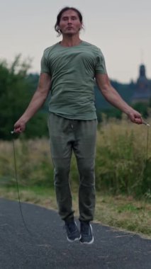 Atletik bir adam, atlama halatı egzersizleri yapıyor. Manzaralı bir yolda, zindelik ve çeviklik sergiliyor. Ağır çekim. Yüksek kalite 4k görüntü