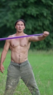 Kaslı bir birey, sakin ve sakin bir açık hava ortamında çeşitli direnç bandı egzersizleri sergiliyor. Ağır çekim. Yüksek kalite 4k görüntü