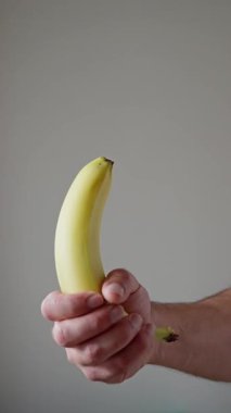 Karşıtlık için basit bir arkaplan ile olgunlaşmış bir muzu sıkıca kavrayan bir elin ayrıntılı bir yakın çekimi