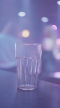 Temiz bir içki bardağı renkli ışıklandırması ve bulanık arkaplanı olan modaya uygun bir barda oturarak canlı bir hava yaratıyor. Yüksek kalite 4k görüntü