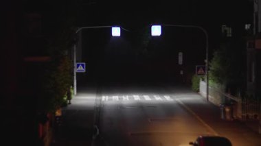 Boş bir caddede, aydınlatılmış trafik işaretleri ve yaya geçitlerinin yer aldığı sakin bir gece sahnesi.