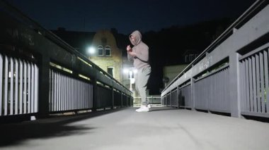 Genç bir adam, gece bir köprüde dövüş sanatları hareketleri yapıyor. Gücünü ve yoğun dikkatini gösteriyor. Ağır çekim. Yüksek kalite 4k görüntü