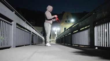 Bir insan, dayanıklılığını ve uygunluğunu vurgulamak için geceleri köprüde direnç bandı egzersizleri yapıyor.