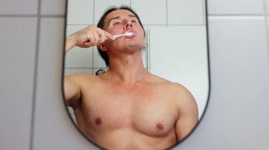 Bir adam banyo aynasında dişlerini fırçalar, sabah rutinini gösterir ve sağlık için hijyenini gösterir.