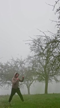 Sisli bir meyve bahçesinin ortasında hareketli ve enerjik hareketler yapan aktif ve sağlıklı bir yaşam tarzı sergileyen bir insan. Ağır çekim. Dövüş sanatları eğitimi. Yüksek kalite 4K görüntü.