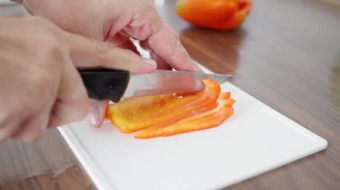 Usta bir şef titizlikle taze turuncu bir dolma biberi büyük bir titizlikle el değmemiş beyaz bir kesme tahtasına dilimliyor.