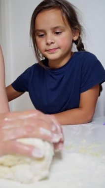 Bir çocuk ilginç bir şekilde bir yetişkinle hamur yoğurmaya katılır ve tatlı bir anı yakalar. Ağır çekim. Dikey görünüm. Yüksek kalite 4k görüntü