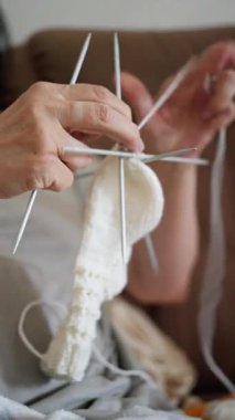 Yumuşak, beyaz bir çorabı ustalıkla ören ellerin yakın çekimi. Etrafında birden fazla iğne ve karmaşık desenler var.
