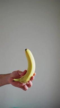 Ağır çekim. Beyaz Arkaplanda Muz Döndürme ve Döndürme Havada Askıya Alındı ve Beyaz Arkaplanda Bir Erkek El Tarafından Yakalandı, İzole Edildi. Dikey video.