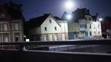 Parlak bir ayın aydınlattığı kentsel evlerin huzurlu gece manzarası, gece vakti sokak ışıklarını gösteriyor.