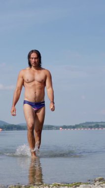 Parlak güneşli bir günde, berrak, parıldayan suda yürüyen bir adam kumsal atmosferinin tadını çıkarıyor.