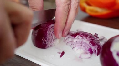 Eller, renkli sebzelerle çevrili beyaz bir tabakta canlı kırmızı bir soğanı ustalıkla kesiyor. Ağır çekim. Yüksek kalite 4k görüntü