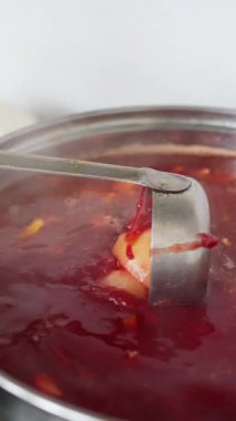 A closeup shot of a ladle expertly scooping a vibrant, rich red soup brimming with a variety of ingredients