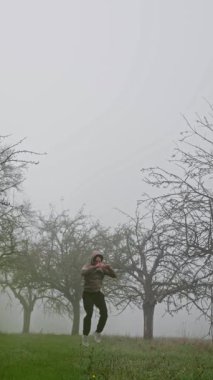 Sisli bir meyve bahçesinde coşkuyla zıplayan bir insan neşe ve canlılık duygusunu tamamen somutlaştırıyor. Yüksek kalite 4k görüntü