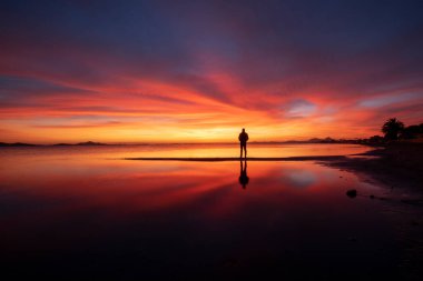 Los Urrutias sahilinde, Mar Menor, Cartagena 'da, denizin sakin sularında yansıyan bulutlar ve güneşi izleyen bir adamın silueti ile birlikte Idyllic turuncu gün doğumu.