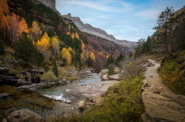 Autumn landscape in the Ordesa y Monte Perdido national park in the Pyrenees, in Huesca, Spain, where you can see a path for hikers and a blue river clipart