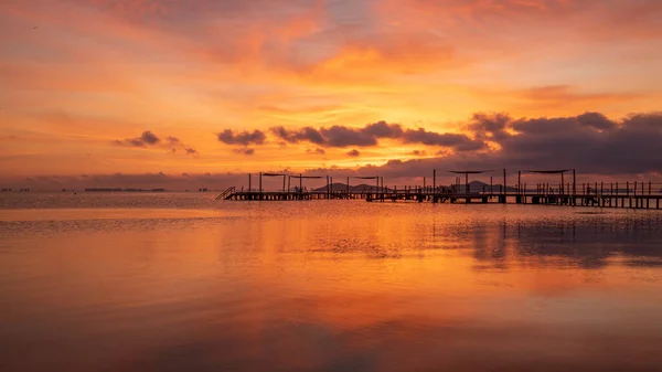 Idyllic orange sunrise on the beach of Los Urrutias, in the Mar Menor, Cartagena, Region of Murcia with the clouds reflecting in the calm waters of the sea and a wooden walkway in the background