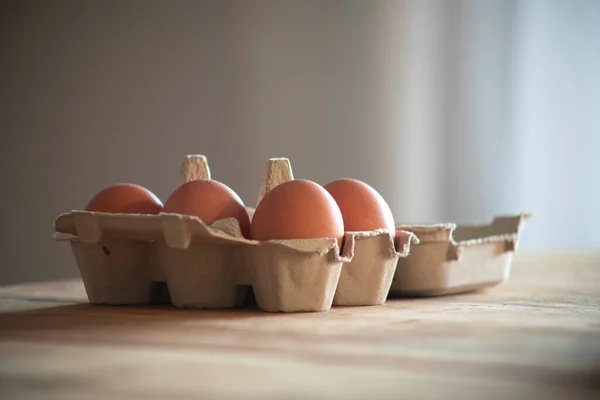 Half dozen eggs in a carton box on naturally lit wooden table