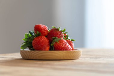 Set of strawberries on wooden plate on the table in a well lit kitchen