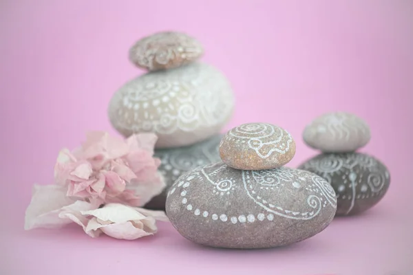 Zen style stacked stones with white line drawings about the universe. there is a pink flower next to the stones on a pink background that transmits calm and tranquility