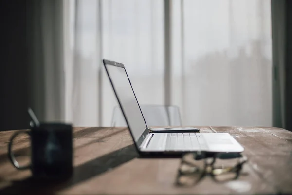 stock image Laptop on a wooden table, a cup of coffee, glasses and a mobile, in a warm and comfortable light environment