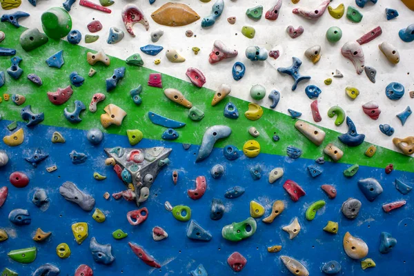Detail of a vertical wall of an indoor climbing wall with holds of different colors to practice climbing