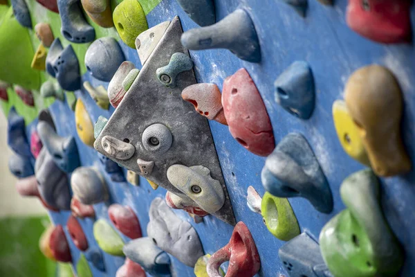 Detail of a vertical wall of an indoor climbing wall with holds of different colors to practice climbing