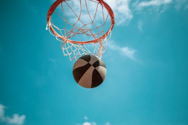 Aşağıdan görülen basketbol potası mavi gökyüzü ve bir smaç topu