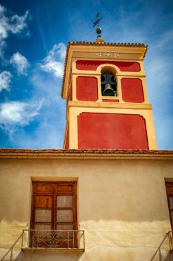 Librilla, Murcia 'daki Parroquia de San Bartolome' un bordo çan kulesi eski bir evin ön cephesinden çıkıyordu.