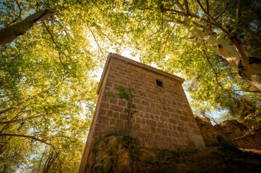 Slender tower of the Templars in the Fuentes del Marques area in Caravaca de la Cruz, Murcia, Spain among leafy trees clipart