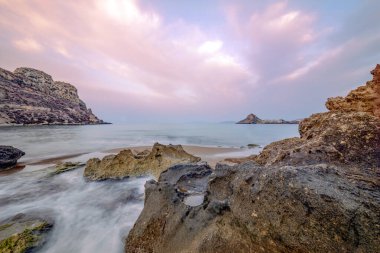 İspanya, Murcia Bölgesi, Aguilas Playa Amarilla 'daki ince kum ve kaya plajları, şeffaf sular ve arka planda uzun süre çekilen Isla del Fraile