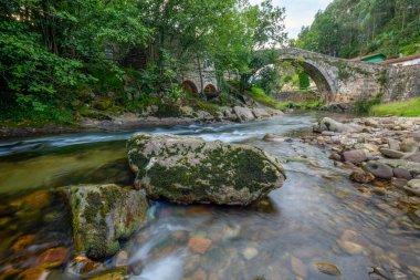 Medieval semicircular arch bridge over the Miera river, Lirganes, Cantabria, Spain, seen from the riverside clipart