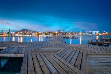 Los Urrutias, Cartagena, Mar Menor, Murcia, İspanya Bölgesi 'ndeki Mar Menor kasabasındaki ahşap kaplıca geçidinde şafakta Los Urrutias' ın arka planında