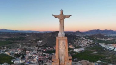 Monteagudo, Murcia, İspanya 'nın etkileyici ortaçağ şatosunun günbatımında arka planda meyve bahçesi ve yukarıda İsa' nın görüntüsü.