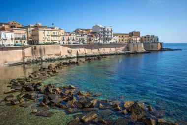 Sicilya, İtalya 'daki Cala Rossa Sahili manzarası, berrak, zümrüt suyu ve arka planda şehir.