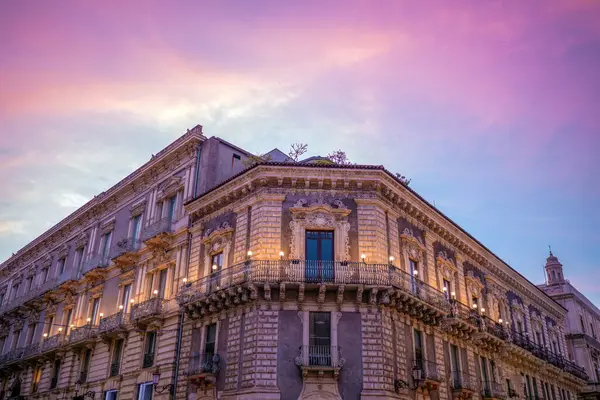 İtalya, Sicilya 'da Via Etnea' da alacakaranlıkta pembe günbatımı gökyüzü ile aydınlatılmış tarihi bir cephe.