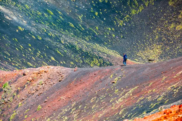 İtalya, Sicilya 'daki Etna Dağı' ndaki bir volkanın kraterinde çok renkli topraklarıyla yürüyen kimliği belirsiz bir adam tasviri.