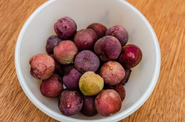 Küçük beyaz bir tabakta mor olgun deniz mahsulü meyvelerine bakıyorum. ahşap arkaplan.