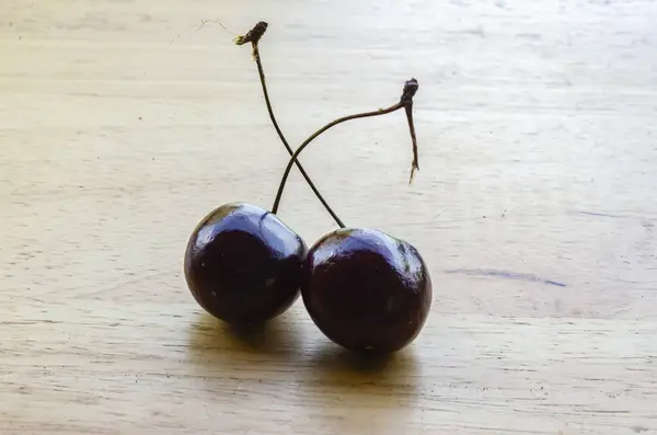 stock image Two burgundy ripe cherries are on the top of a wooden table..