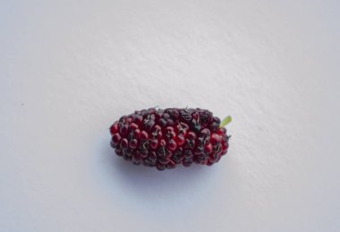 An isolated ripe mulberry is on the surface of a white tile. clipart