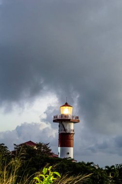 Gecenin geç saatlerinde küçük bir tepenin tepesinde kırmızı ve beyaz bir deniz feneri parlıyor..