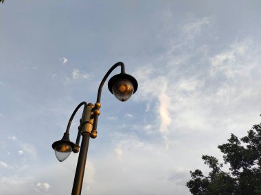 Klasik bir dekoratif sokak lambası silueti alacakaranlıkta ya da şafakta yumuşak bulutlu mavi gökyüzüne karşı. Kentsel tasarım, güvenlik ve klasik ışıklandırmayı temsil eder