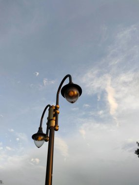 Klasik bir dekoratif sokak lambası silueti alacakaranlıkta ya da şafakta yumuşak bulutlu mavi gökyüzüne karşı. Kentsel tasarım, güvenlik ve klasik ışıklandırmayı temsil eder