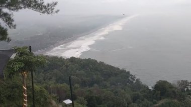 Bereketli yeşil bitki örtüsü ve dalgaları açık gökyüzü altında kayalık kıyıya vuran kıyı kayalıkları. Doğa, manzara veya seyahat temalı görsel içerik için ideal