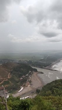 Puslu vadi manzarası, ormanlık tepeler, kıvrımlı nehir ve bulutlu gökyüzünün altındaki uzak yerleşim yerleri. Doğa, manzara veya seyahat temalı görsel içerik için ideal