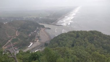Puslu vadi manzarası, ormanlık tepeler, kıvrımlı nehir ve bulutlu gökyüzünün altındaki uzak yerleşim yerleri. Doğa, manzara veya seyahat temalı görsel içerik için ideal