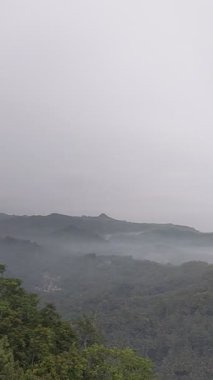 Puslu vadi manzarası, ormanlık tepeler, kıvrımlı nehir ve bulutlu gökyüzünün altındaki uzak yerleşim yerleri. Doğa, manzara veya seyahat temalı görsel içerik için ideal